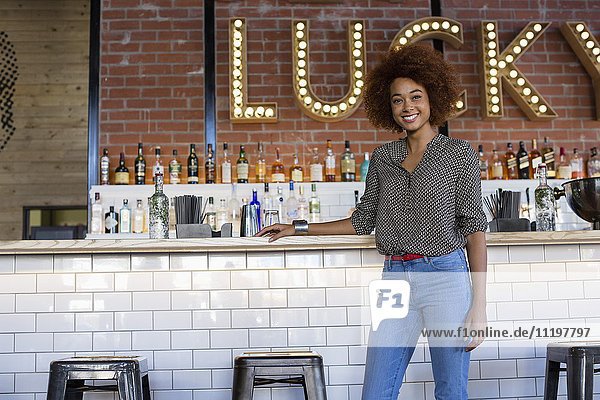 Portrait of happy young woman standing at bar counter