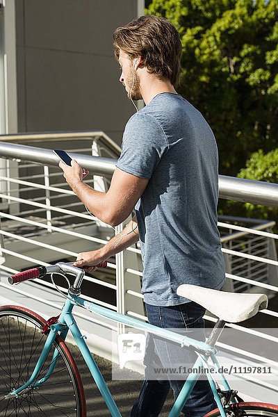 Junger Mann mit Handy und Fahrrad im Freien