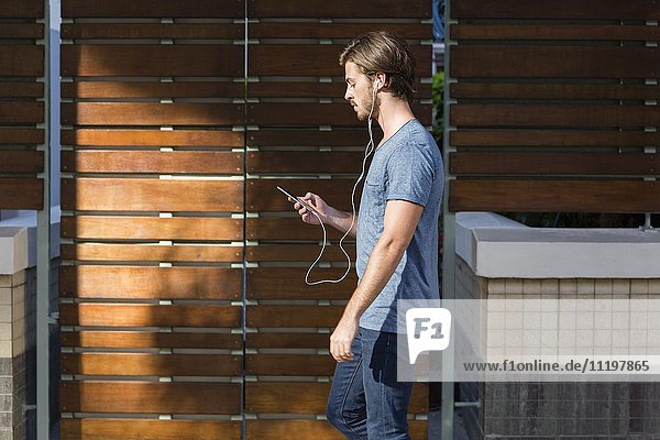 Junger Mann hört Musik auf dem Smartphone während des Spaziergangs