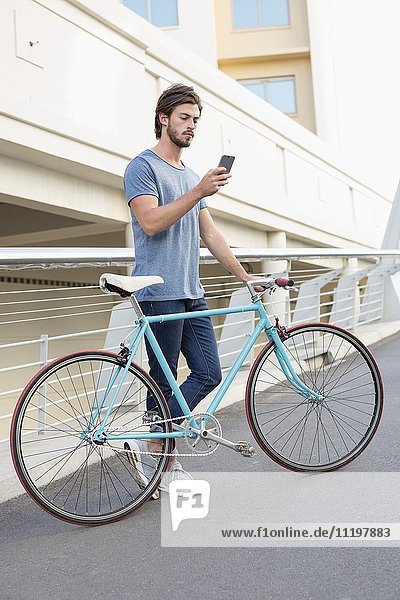 Junger Mann mit Handy und Fahrrad im Freien