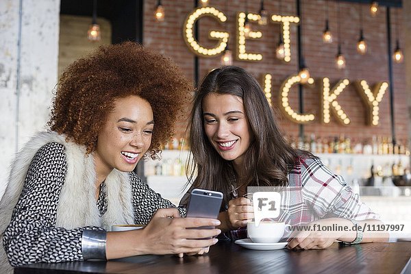 Freundinnen nutzen ein Smartphone mit Kaffee im Cafe