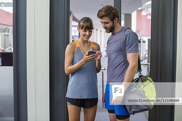 Junges Paar beim Blick auf ein Smartphone außerhalb des Fitnessstudios