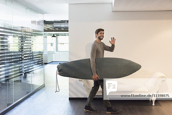 Glücklicher junger Mann mit Surfbrett zu Hause