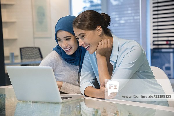 Zwei glückliche Geschäftsfrauen beim Blick auf einen Laptop im Büro