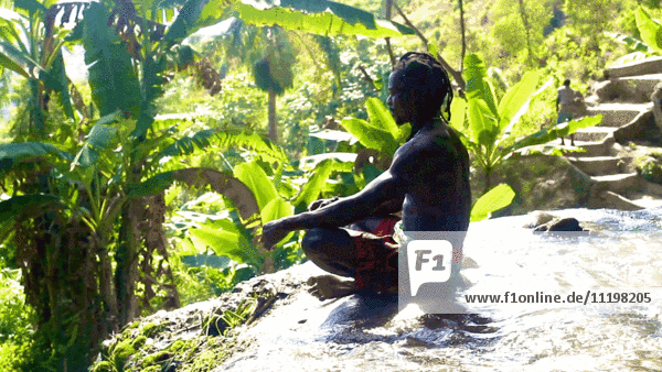 Mann meditiert am Rande eines tropischen Wasserfalls