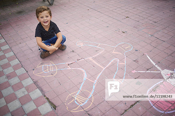 Hispanic boy with chalk drawing on sidewalk