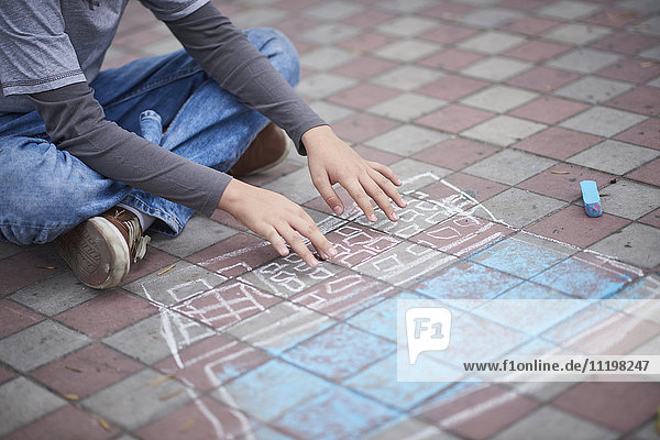 Hispanic boy typing on chalk laptop on sidewalk