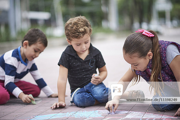 Hispanic boys and girl drawing with chalk on sidewalk