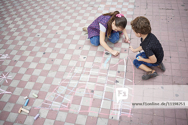 Hispanischer Junge und Mädchen zeichnen mit Kreide auf dem Bürgersteig