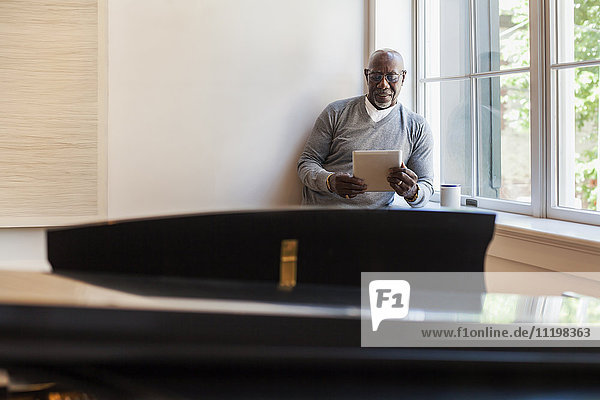 Mann benutzt digitales Tablet in der Nähe des Fensters hinter dem Klavier
