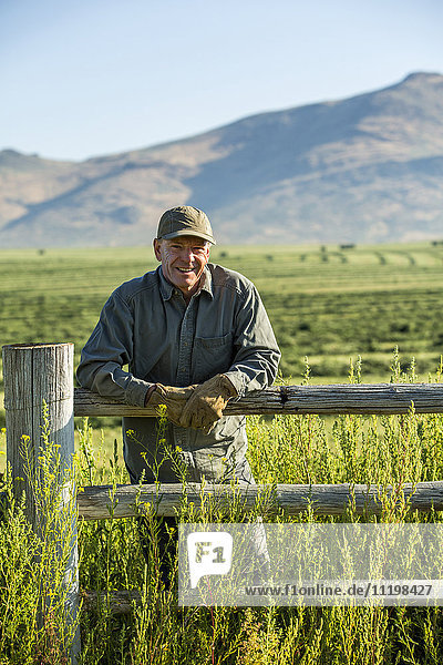 Kaukasischer Bauer mit Handschuhen  der sich an einen Holzzaun lehnt