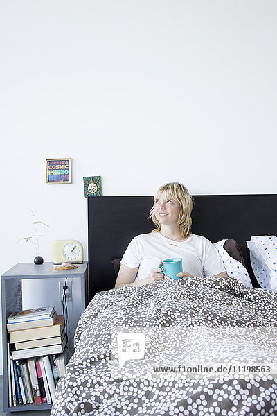 Caucasian woman drinking coffee in bed