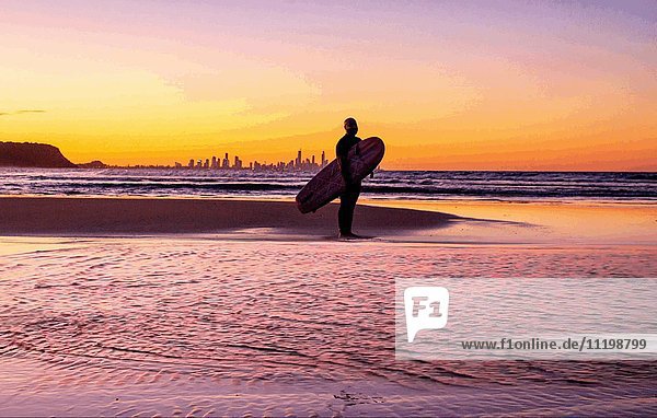 Silhouette eines Surfers am Strand mit Skyline im Hintergrund bei Sonnenuntergang  Currumbin Beach  Gold Coast  Queensland  Australien