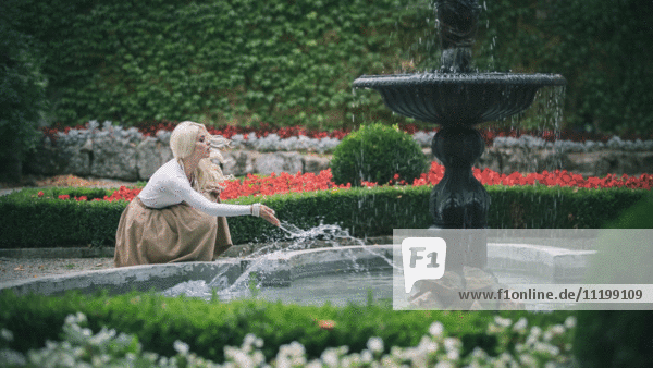 Attraktive junge erwachsene Frau spritzt Wasser am Brunnen