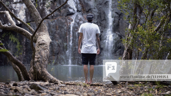 Mann am Wasserfall stehend,  Rückansicht
