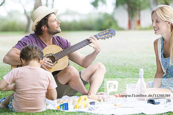 Man playing acoustic guitar next to wife and son