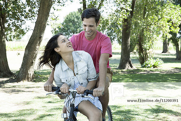 Junges Paar beim Radfahren zusammen mit der Freundin sitzend im Damensattel auf der Querlatte
