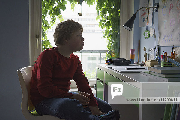 Junge liest Alphabete  während er am Schreibtisch im Zimmer sitzt.