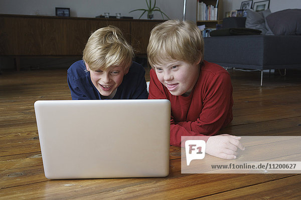 Smiling brothers using laptop while lying on hardwood floor at home