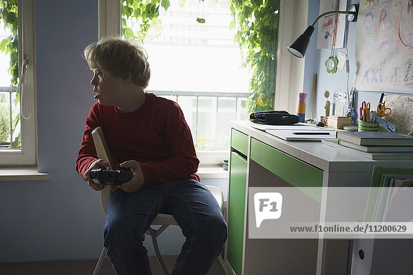 Behinderter Junge  der ein Videospiel spielt  während er auf einem Stuhl im Zimmer sitzt.
