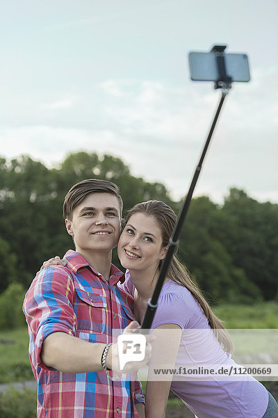 Fröhliches junges Paar nimmt Selfie durch Einbeinstativ im Park mit