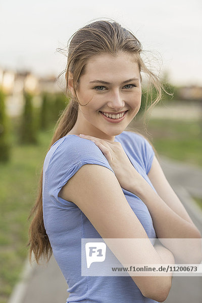 Portrait of cheerful young woman standing with arms crossed at park