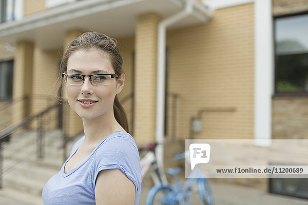 Smiling young woman wearing eyeglasses standing against house