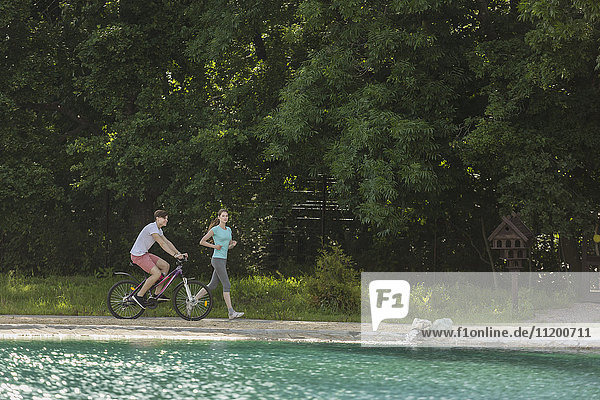 Woman jogging while man cycling by lake in park
