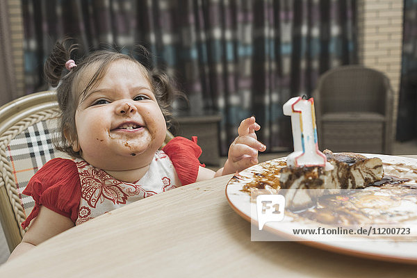 Cute girl with messy face having birthday cake at table