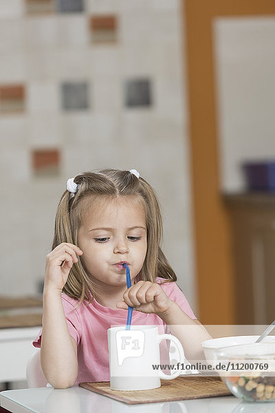 Girl drinking milk in mug while having breakfast at home