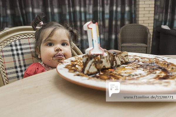 Porträt eines süßen Mädchens  das bei einem Geburtstagskuchen am Tisch die Zunge herausstreckt.