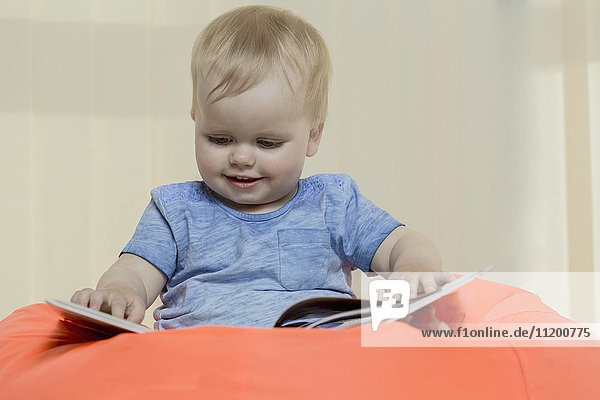 Nahaufnahme des süßen lächelnden Mädchens beim Lesen eines Buches während es zu Hause auf einem Bohnensack sitzt.