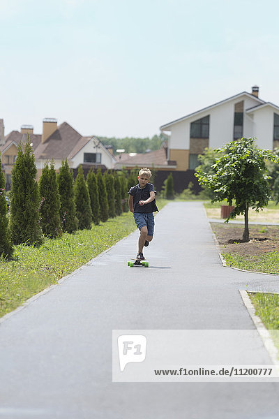 Boy skateboarding on road amidst trees against houses in town