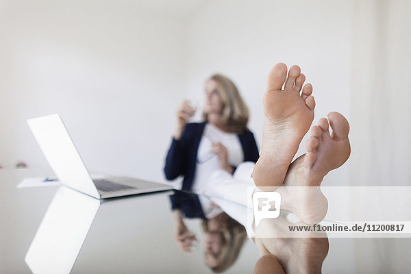 Frau mit gekreuzten Beinen am Knöchel mit Laptop auf dem Tisch im Büro