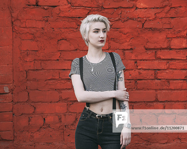 Confident young woman standing against red brick wall