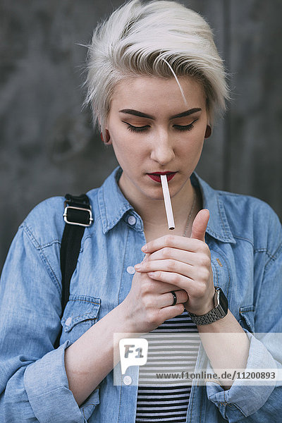 Junge modische Frau raucht Zigarette  während sie draußen steht.