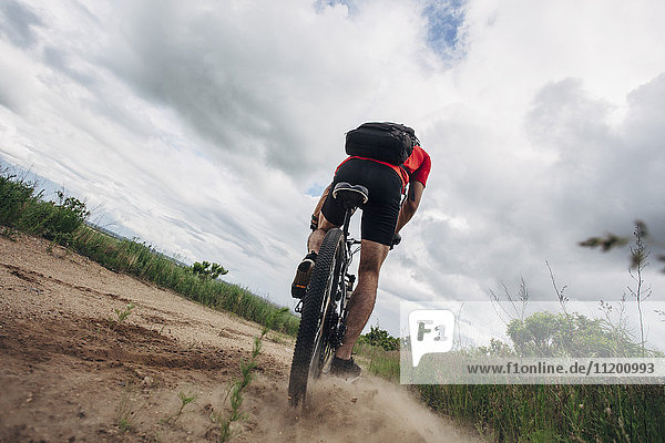 Low angle view of man riding mountain bike on dirt road against cloudy sky