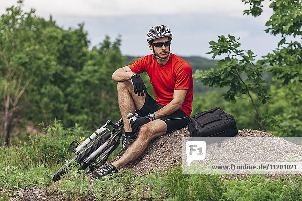 Tired mountain biker sitting on ground against trees