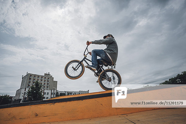 Low angle view of teenage boy performing stunt on ramp against cloudy sky