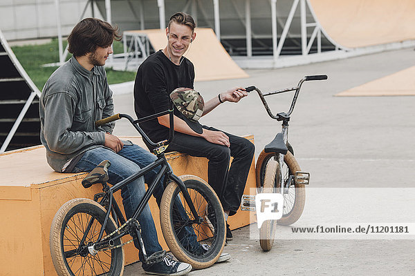 Cheerful friends resting on seat with bicycles at skateboard park