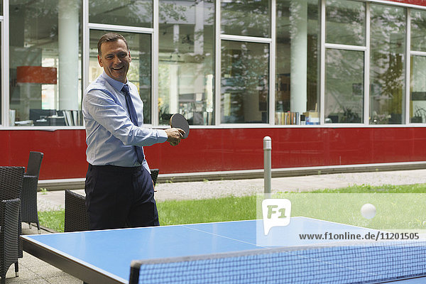 Zuversichtlicher  fröhlicher Geschäftsmann beim Tischtennisspielen im Kreativbüro