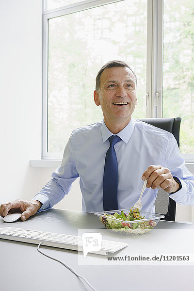 Smiling businessman having salad at desk in creative office