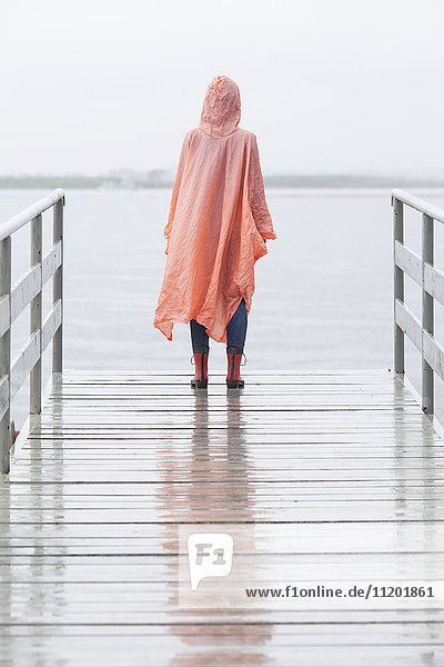 Rückansicht der Frau im Regenmantel am Steg während der Regenzeit