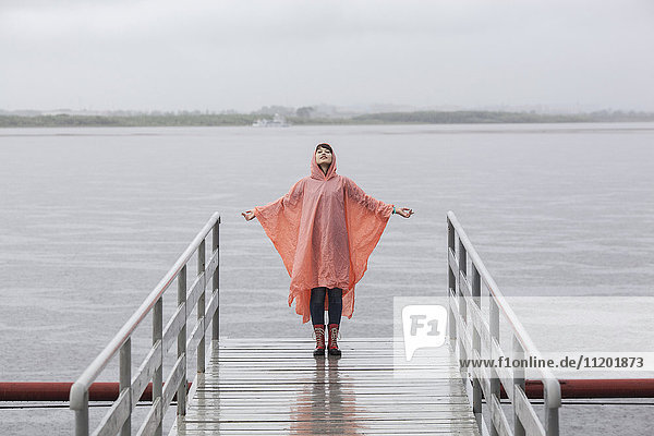 Woman wearing raincoat enjoying rainy season while standing on jetty