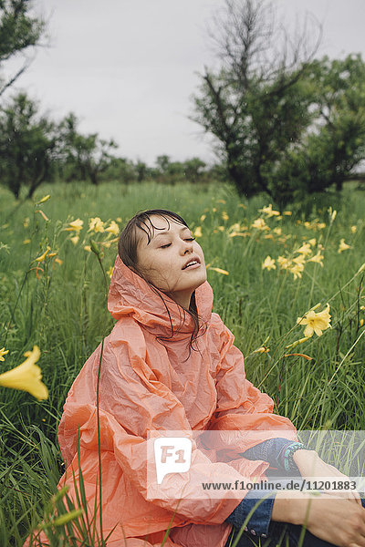 Junge Frau entspannt inmitten gelb blühender Pflanzen während der Regenzeit