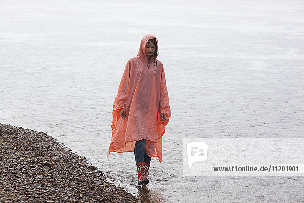 Frau im Regenmantel beim Spaziergang am Seeufer in der Regenzeit