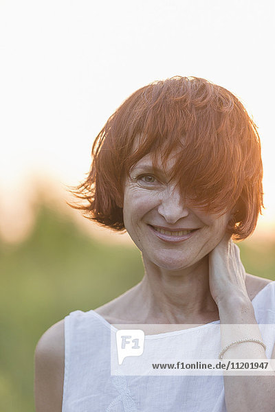 Portrait einer lächelnden Frau mit kurzen braunen Haaren  die im Freien stehen