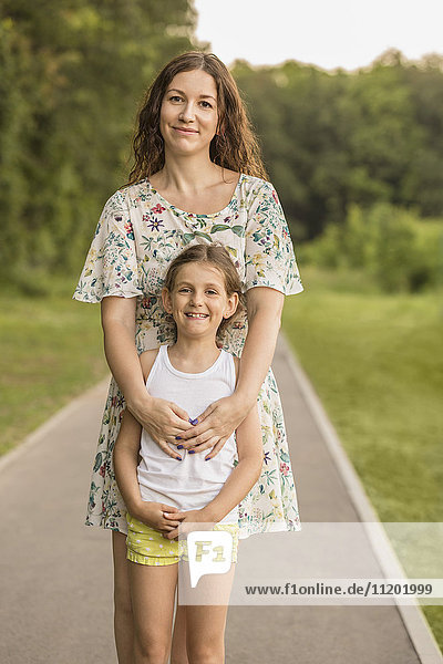 Portrait of beautiful woman and daughter standing on footpath at park
