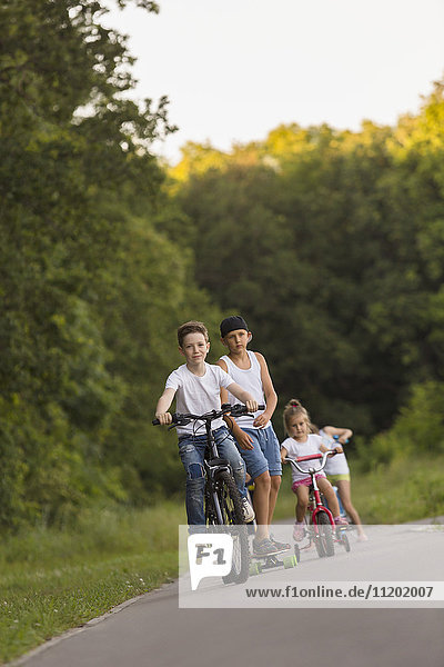 Siblings cycling on road against trees at park