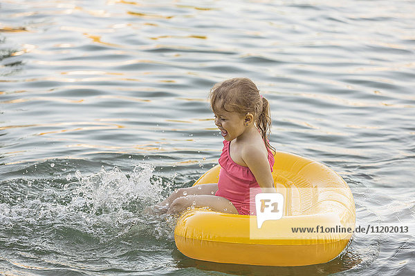 Fröhliches Mädchen sitzt auf dem Floß und spielt im See.